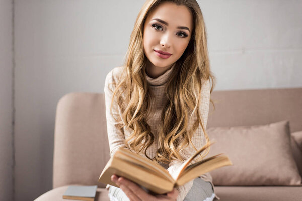 beautiful young woman reading book on cozy couch at home