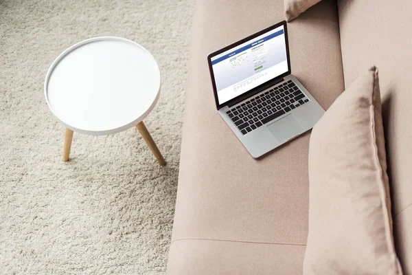高角度的笔记本电脑站在舒适的沙发上与 Facebook 网站在屏幕上 — 图库照片