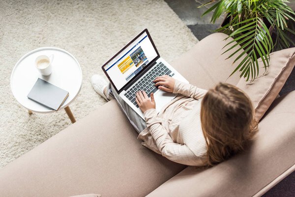 high angle view of woman at home sitting on couch and using laptop with booking website on screen