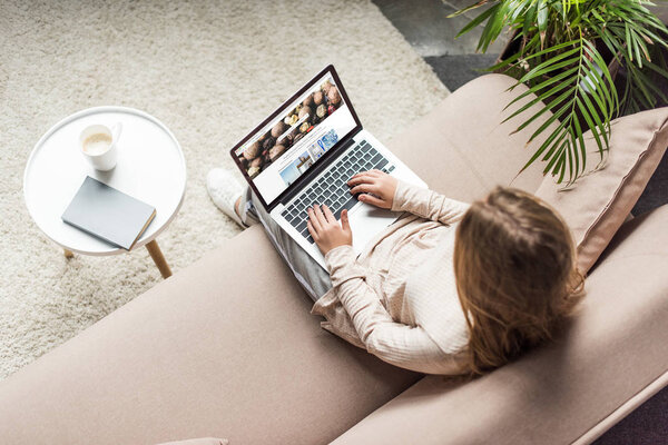 high angle view of woman at home sitting on couch and using laptop with shutterstock homepage on screen