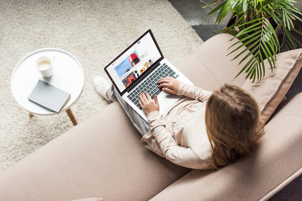 high angle view of woman at home sitting on couch and using laptop with ebay website on screen