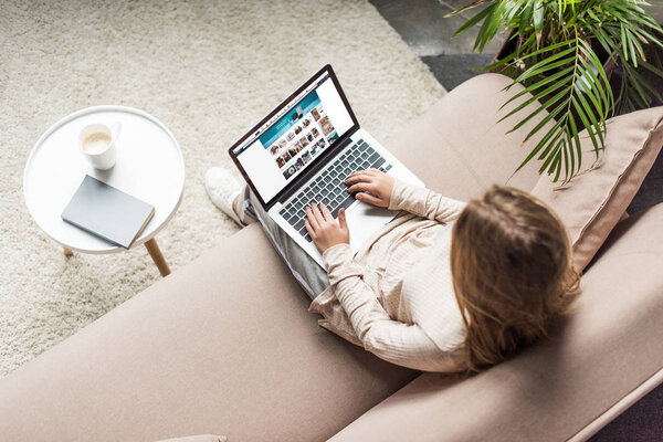 high angle view of woman at home sitting on couch and using laptop with amazon website on screen
