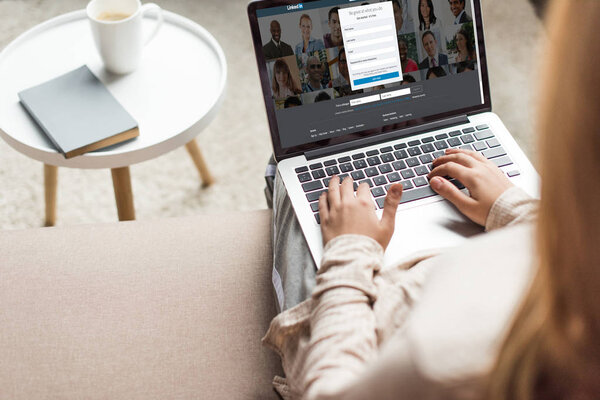 cropped shot of woman at home sitting on couch and using laptop with linkedin website on screen