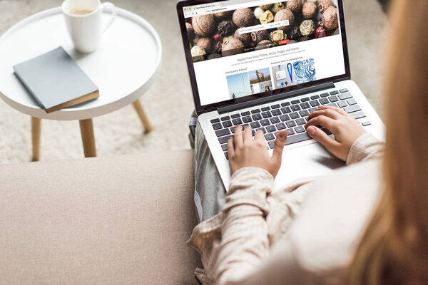 cropped shot of woman at home sitting on couch and using laptop with shutterstock website on screen