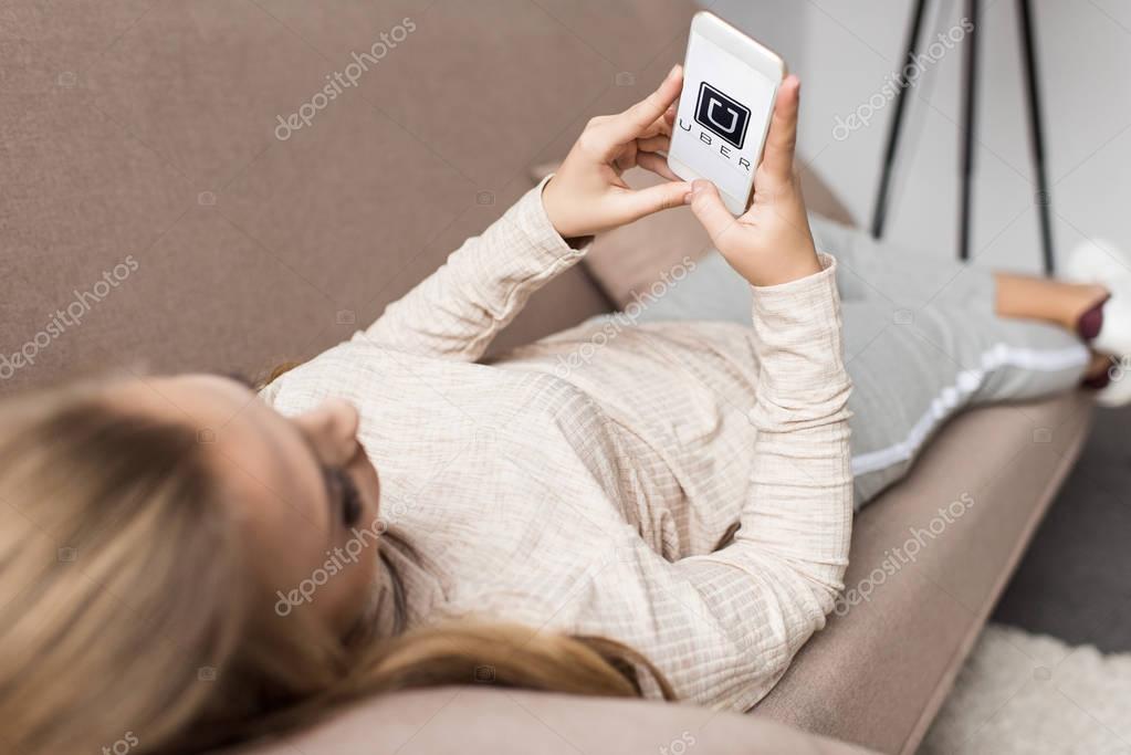 Woman on couch using smartphone with uber logo on screen