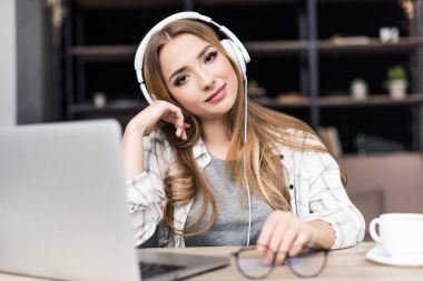 mutlu genç kadın kameraya bakıyor ve işyerinde bir kulaklık ile müzik dinleme