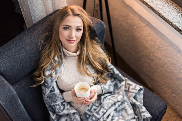 high angle view of beautiful young woman drinking coffee in cozy chair