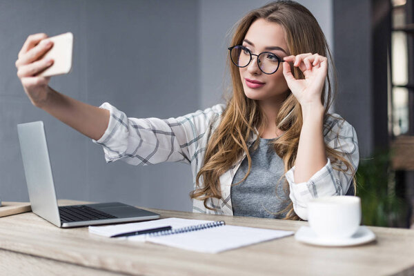 happy young businesswoman taking selfie at workplace