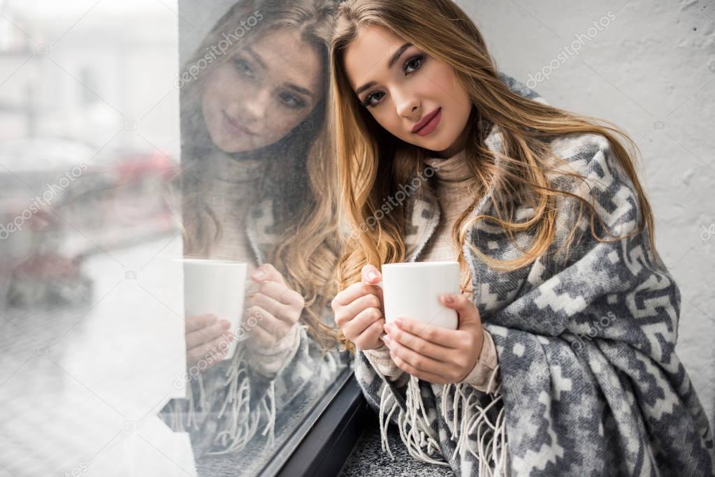 beautiful young woman drinking coffee while leaning on window