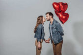 a fiatal pár képes megcsókolni, míg férfi piros szív alakú lufi, elszigetelt szürke gazdaság oldalnézete 