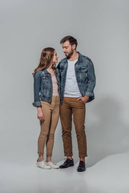 Genç çift denim ceket gri izole birbirlerine bakarak gülen tam uzunlukta görünümü