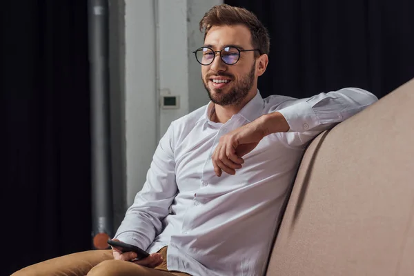 Handsome Smiling Young Man Eyeglasses Holding Smartphone Looking Away Home — Stock Photo, Image