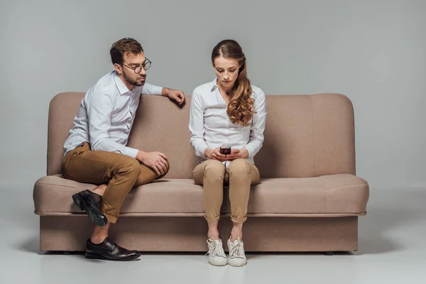 Ung Kvinna Med Smartphone Medan Pojkvän Sitter Nära Soffan Isolerad — Stockfoto