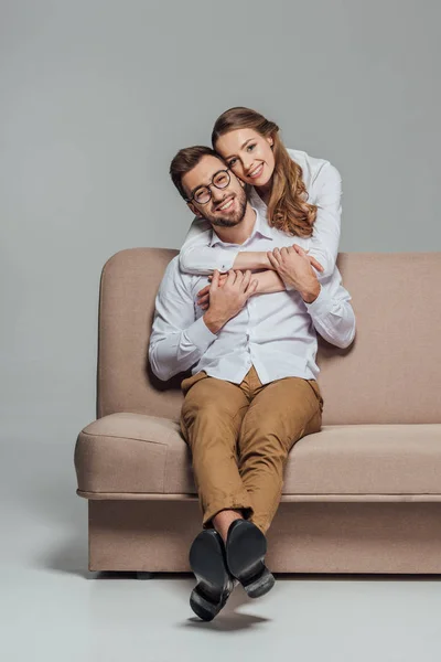 Alegre Jovem Casal Abraçando Sofá Sorrindo Para Câmera Isolada Cinza — Fotografia de Stock