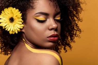 Şehvetli Afro-Amerikan olan kadın sanatsal makyaj ve saç üzerinde turuncu arka plan izole gerbera