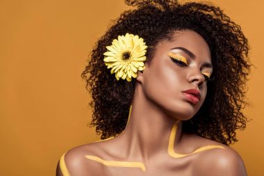 Şehvetli Afro-Amerikan olan kadın sanatsal makyaj ve saç üzerinde turuncu arka plan izole gerbera