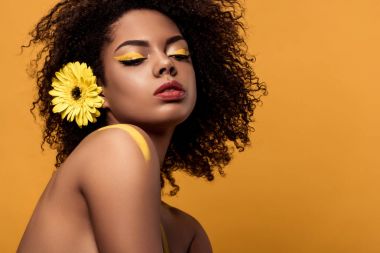 Genç Afro-Amerikan kadın sanatsal makyaj ve saç üzerinde turuncu arka plan izole gerbera ile ihale