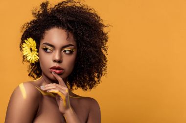 Sanatsal makyaj ve saç gerbera genç parlak Afrikalı-Amerikalı kadın yüzü üzerinde turuncu arka plan izole tarafından el tutar