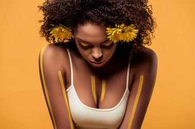 Young sensual african american woman with artistic make-up and gerbera in hair isolated on orange background