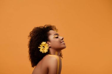 Sanatsal makyaj ve saç üzerinde turuncu arka plan izole gerbera ile şık Afrikalı-Amerikalı kadın