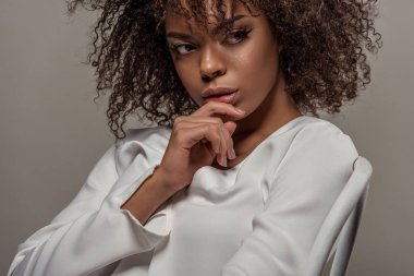 Gri arka plan üzerinde izole dudaklarında parmak ile Beyaz gömlekli şehvetli genç Afro-Amerikan kadın