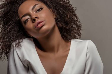 Beyaz gömlek gri arka plan üzerinde izole baştan çıkarıcı bakışla genç Afro-Amerikan kadın