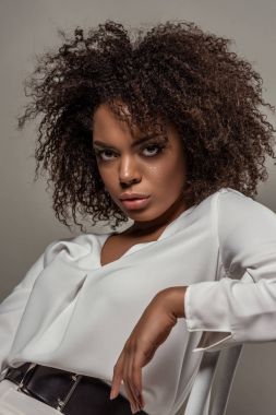 Beyaz gömlek gri arka plan üzerinde izole baştan çıkarıcı bakışla genç Afro-Amerikan kadın