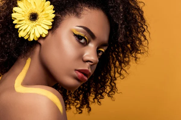 İhale Afro-Amerikan olan kadın sanatsal makyaj ve saç üzerinde turuncu arka plan izole kamera bakarak gerbera
