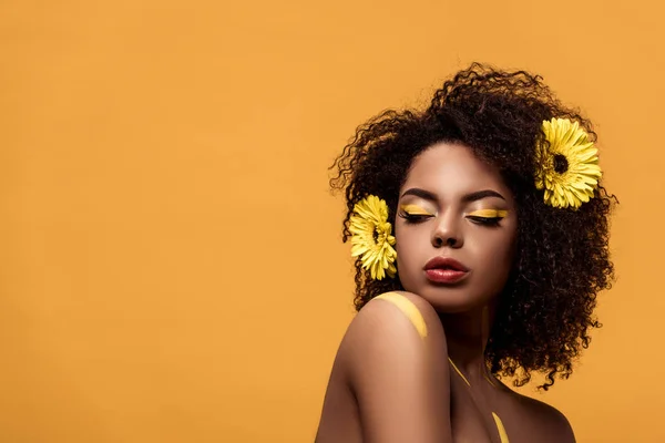 芸術的な化粧と髪がオレンジ色の背景に分離されたガーベラの官能的なアフリカ系アメリカ人女性 — ストック写真