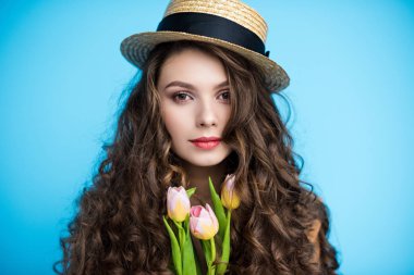 attractive young woman with long curly hair in canotier hat holding beautiful tulips