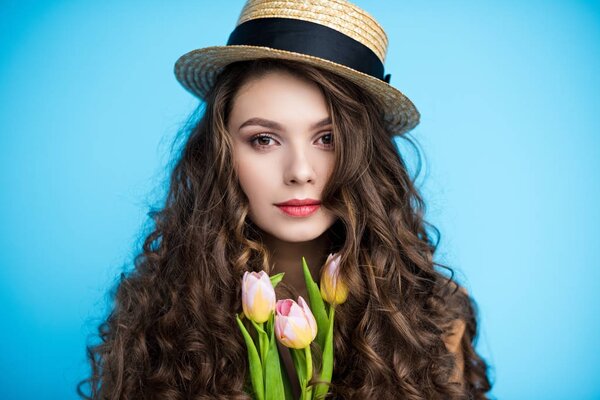 привлекательная молодая женщина с длинными вьющимися волосами в канотье шляпы с красивыми тюльпанами
