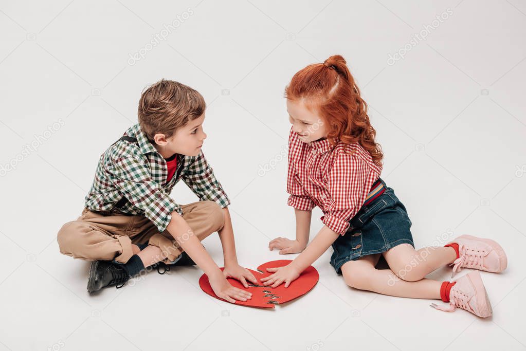 adorable little kids putting parts of broken heart symbol together isolated on grey