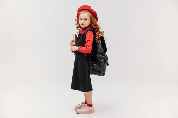 美しい小さな女子高生本とバックパック グレーで隔離赤いベレー帽の側面図 — ストック写真