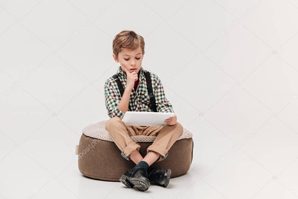 focused little boy sitting and using digital tablet isolated on grey