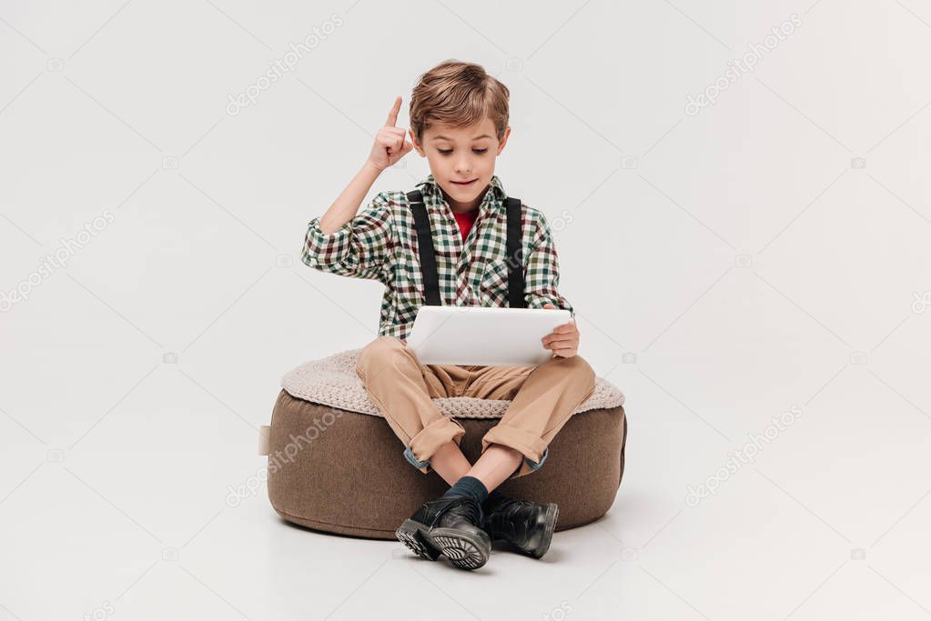 cute little boy using digital tablet and pointing up with finger isolated on grey
