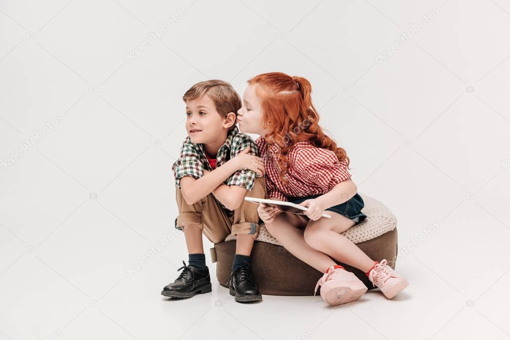 adorable little girl holding digital tablet and able to kiss little boy isolated on grey
