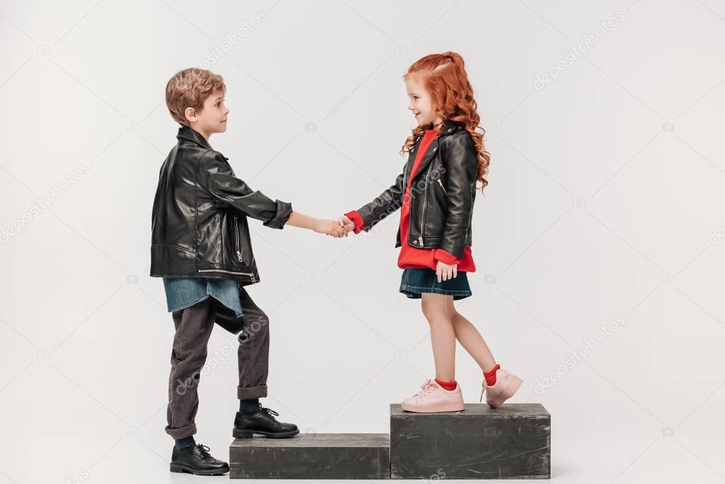 stylish little kids couple holding hands on stairs isolated on grey