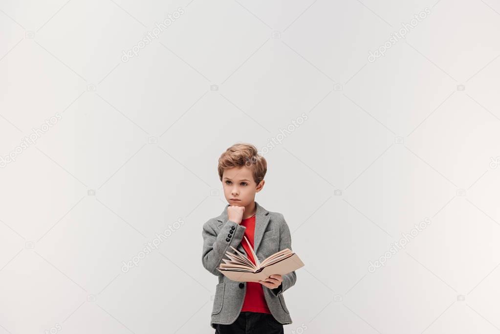 thoughtful little schoolboy with book isolated on grey