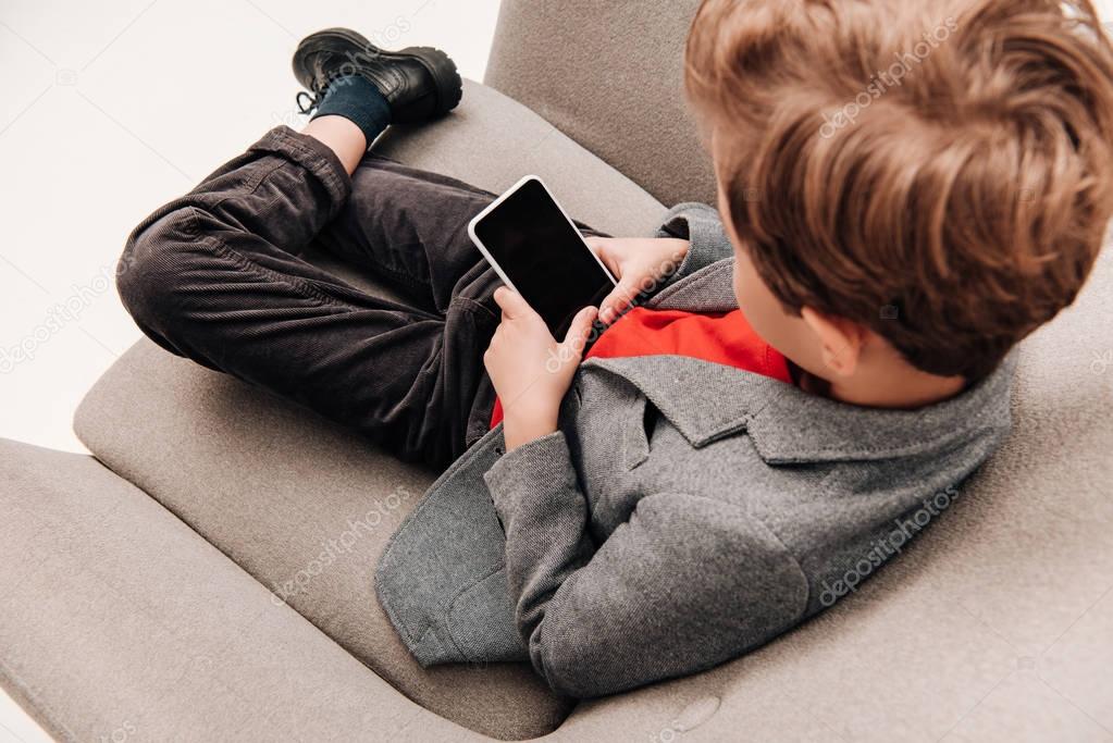 high angle view of stylish little boy using smartphone in armchair
