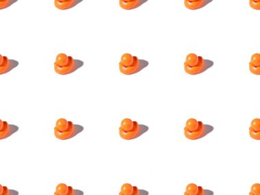 seamless pattern of small orange rubber ducks toys on white clipart