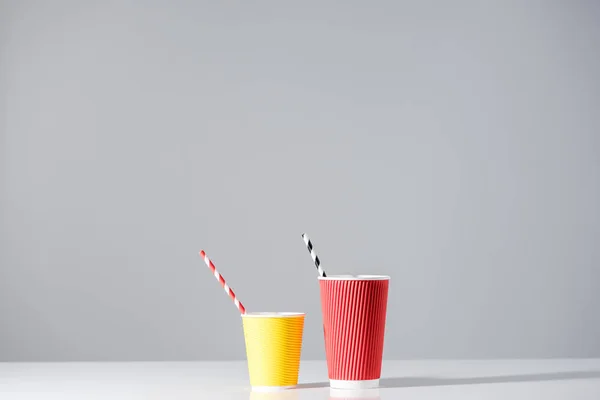 red and yellow paper cups with drinking straws on grey