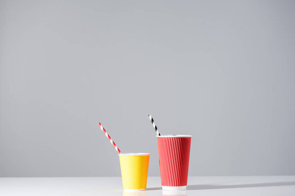 red and yellow paper cups with drinking straws on grey