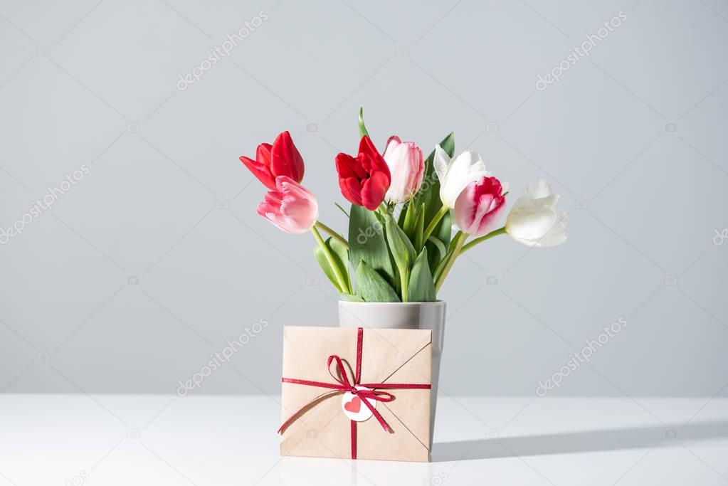 beautiful blooming tulip flowers in vase and envelope on grey