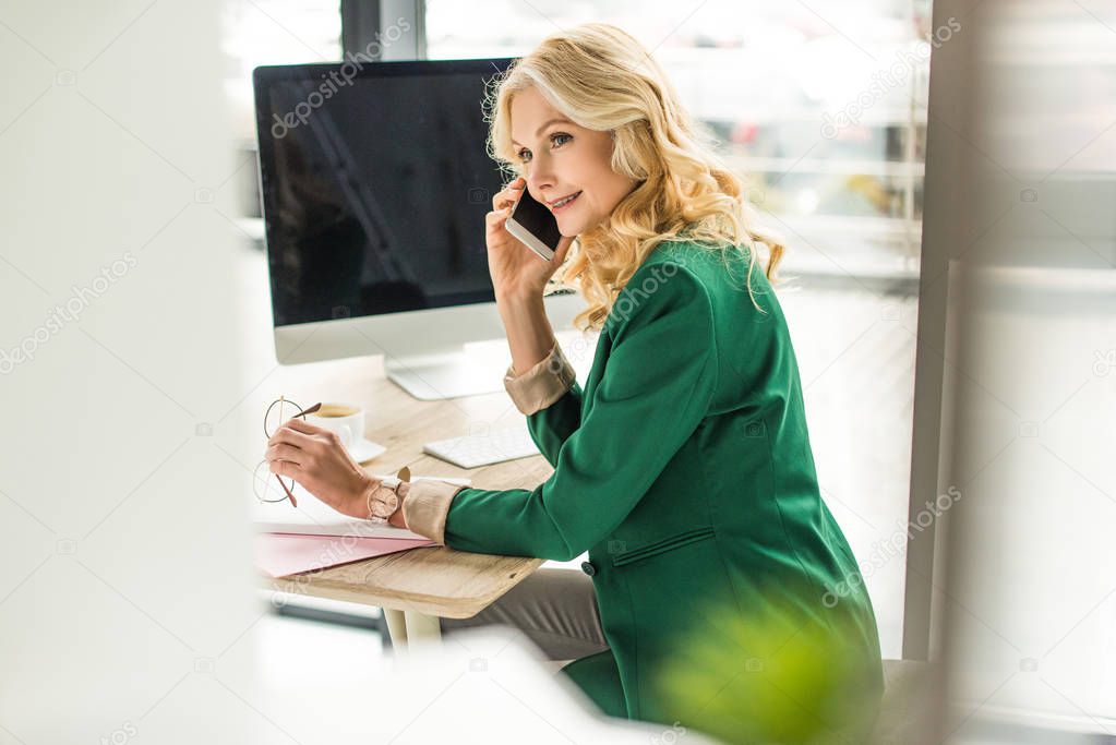 selective focus of beautiful businesswoman talking by smartphone at workplace 