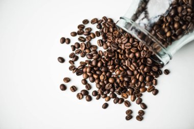 top view of scattered coffee beans from glass bottle isolated on white clipart