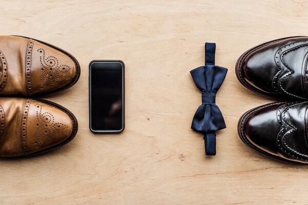 top view of shoes, smartphone and tie bow on wooden surface