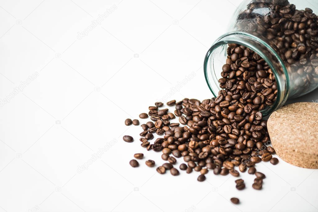 scattered coffee beans from glass bottle and cork isolated on white