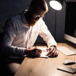 Hombre de negocios escribiendo algo a cuaderno en la oficina por la noche