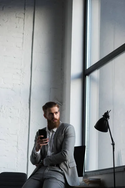 Businessman Holding Smartphone Looking Away — Free Stock Photo