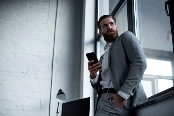 底部的看法英俊的大胡子商人使用智能手机在办公室 并期待远离 — 免费的图库照片